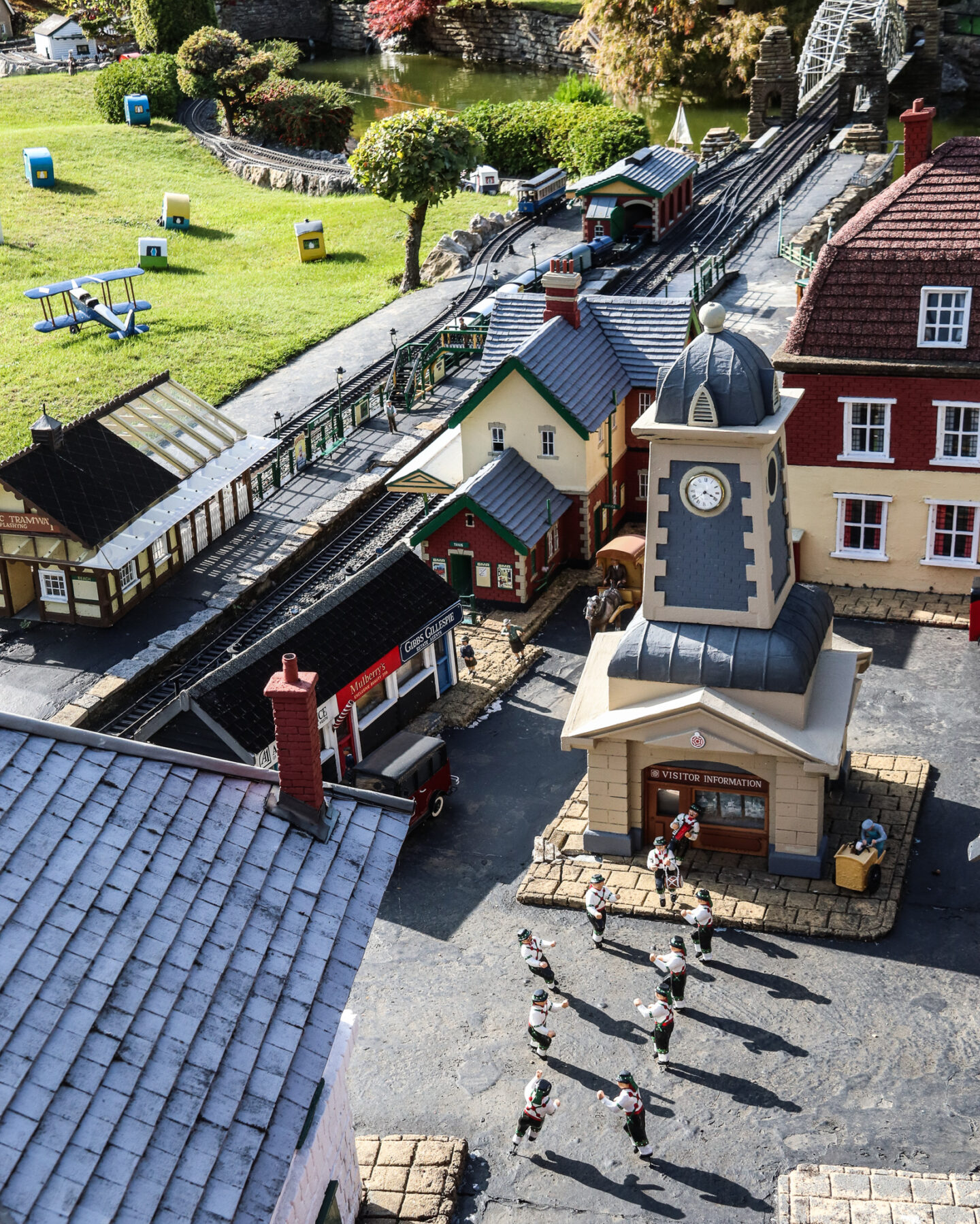 A close up of miniature villagers morris dancing in the village square, close by a model train station. 