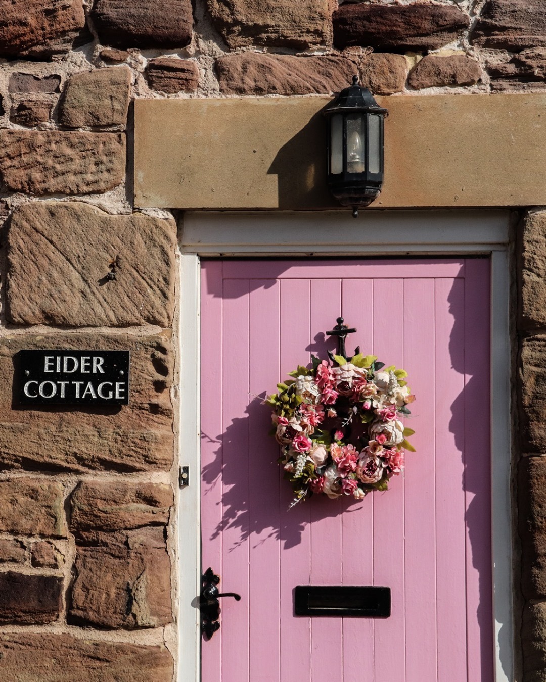 A pink door in Seahouses. There is a floral reef on the door and a sign saying Eider Cottage. It's one of the many fishing cottages that have been repurposed into holiday lettings. It's a great base for visiting the Farne Islands. 