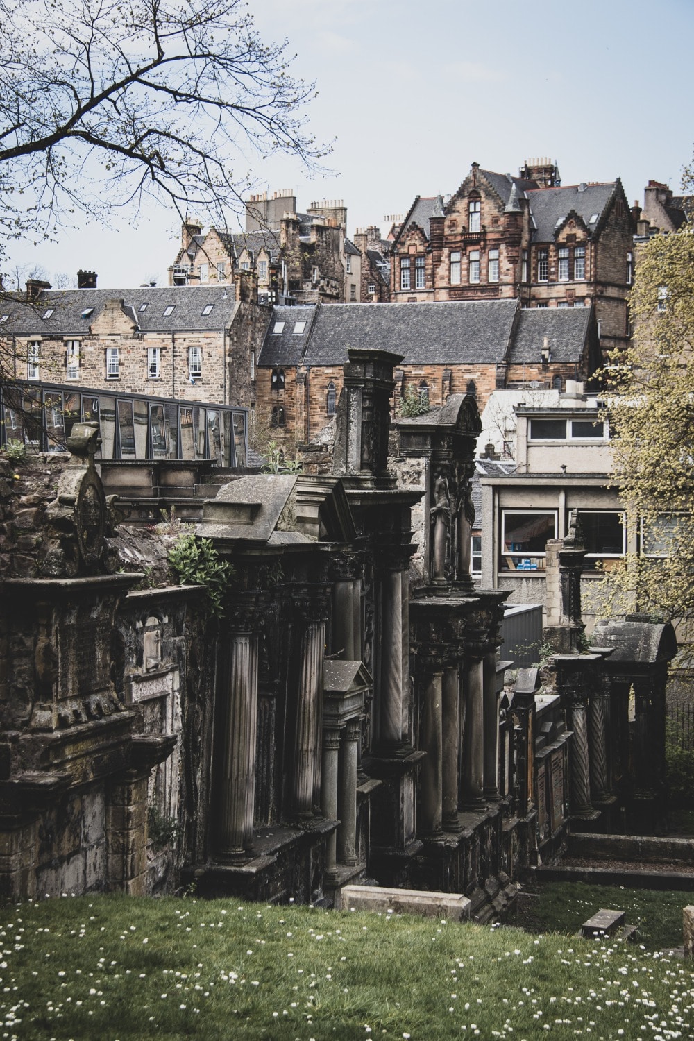 A view of gothic tombstones inside the Greyfriars Kirkyard with a view of buildings in the old town in the distance. 